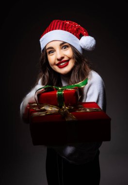 Hediye Tutan Şenlikli Kadın. Noel Baba şapkalı bir kadın elinde hediye tutuyor.