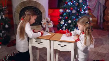 Noel zamanı küçük kızlar. Mutlu küçük kızlar Noel Baba için resim çiziyor.