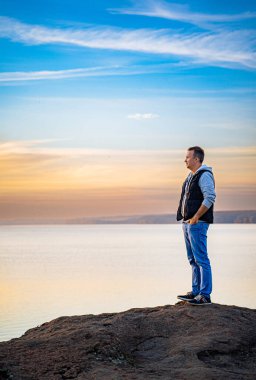 Rocky Outcrop 'tan Huzurlu Manzaranın tadını çıkaran Adam. Bir kayanın üstünde bir su kütlesinin yanında duran bir adam.