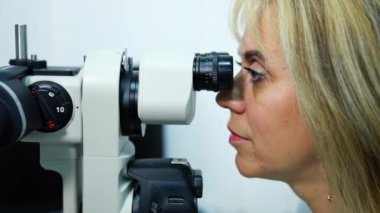 Doktor optik cihazı inceliyor. Klinikteki tıbbi aletler vasıtasıyla görme yeteneğini test eden bir kadının profili..