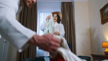 Çekici bir kadın ve bavul hazırlayan bir adam. Beyaz önlüklü bir çift otelde bavula kıyafet koyuyor. Oda çok sıcak. Yolculuk bitiyor.