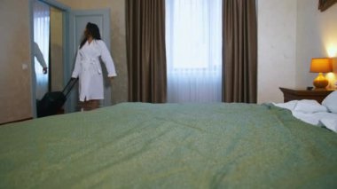 Tatil sırasında sabahlık giyen bir çift. Genç bir kadın ve bavullu bir adam otel odasına giriyor. Bir kadın arabanın çantasını içeri çekiyor..