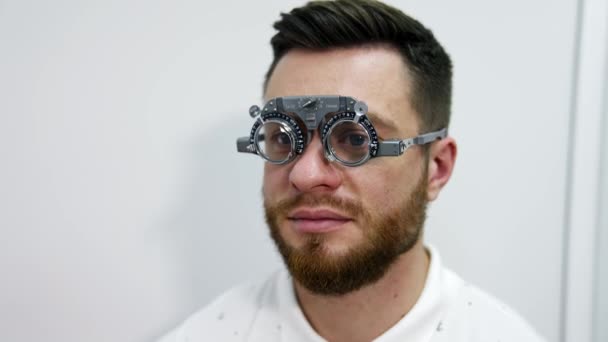 一个人的脸在试镜的框架在眼睛上 病人在诊所用特殊的眼镜检查他的视力 医生把镜片放进试镜架 眼科学 — 图库视频影像