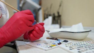 Laboratuvar çalışanı göz protezi boyuyor. Klinikte fırçayla yapay göz yapan kırmızı lateks eldivenler ustası. Yakın plan..
