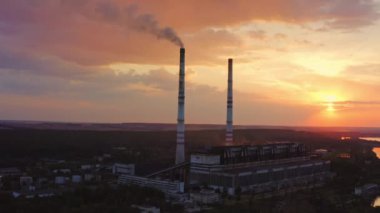 Kırsal kesimde zararlı bir fabrika. Gece gökyüzünde batan güneşli kule boruları olan endüstri. Üretimden çıkan kimyasal duman havayı kirletir. Yukarıdan görüntüle.