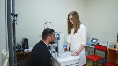 Genç göz doktoru ve hasta. Tıp önlüklü kadın doktor klinikteki özel bir cihazda hastanın gözlerini tedavi ediyor. Yavaş çekim.