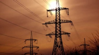 Akşam gökyüzüne karşı iletim hatları. Batan güneşin arka planında kabloları olan yüksek voltajlı elektrik kuleleri. Elektrikli siyah sütunlar.