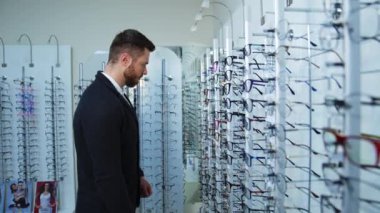 Gözlük mağazasında erkek müşteri. Dükkanda gözlük seçen yakışıklı bir adamın profil görüntüsü. Optik alıcısı.