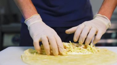 Şef pita ekmeği hazırlıyor. Profesyonel aşçı pidenin içine peynir ve doğranmış salatalık koyuyor. Fast food. Kafkas mutfağı. Yakın plan..