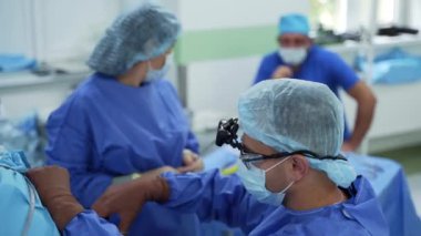 Ameliyathanede ameliyat. Hemşire ameliyathanede cerraha asistanlık yapıyor. Koruyucu üniformalı sağlık görevlileri bir operasyon düzenliyor..