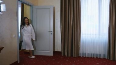 Oteldeki mutlu kadın. Beyaz sabahlık giymiş neşeli genç bir kadın elinde bavulla odaya giriyor ve kocasına gösteri yapıyor..