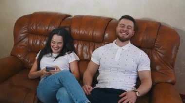 Kanepede mutlu genç bir çift. Genç bir kadın akıllı telefona bakıyor ve evdeki kanepede otururken kocasıyla konuşuyor. Aşık bir çift otelde dinleniyor..