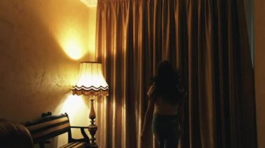Mutlu iyimser genç bayan pencereyi açıyor. Gülümseyen kız pencereye doğru koşuyor ve lüks otel odasında karanlık perdeleri açıyor..