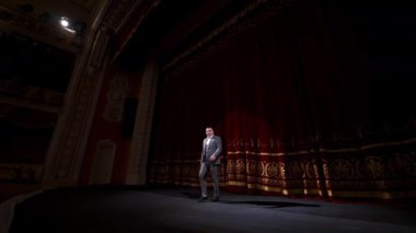 Tiyatro sahnesinde takım elbiseli bir aktör. Erkek komedyen sahnede fıkra anlatır ve dans eder. Sahnede neşeli bir sanatçı.