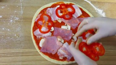 Restoranda pizza yapmak. Pizza pişirmek. Şefin elleri pizzanın üzerine domates parçaları yayıyor. Üst görünüm.