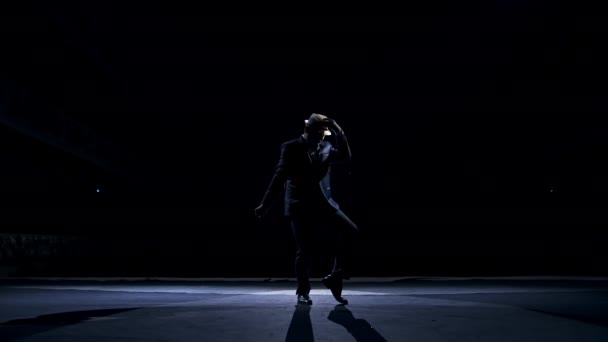 在舞台上表演滑稽舞蹈的演员 一个穿着服装 戴着帽子 在黑暗的背景下跳舞的男人的轮廓 在现场欣赏表演 — 图库视频影像