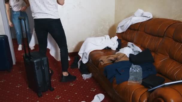 一对年轻夫妇在酒店房间里 度假旅行后 男人和女人都带着衣服 两个旅行箱 沙发上的衣服 旅游夫妇冒险生活方式 — 图库视频影像