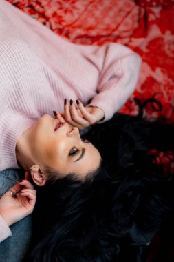 Bir kadın, rahat pembe bir süveter giyerken, sükunetle çevrili bir yatağa nazikçe uzanır..
