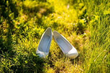 Zarif bir çift beyaz ayakkabı canlı bir zümrüt tarlasında duruyor. Moda ve doğa arasındaki uyumu somutlaştırıyor..