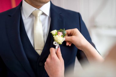 Üstün sanatsal bir gösteriyle takım elbiseli bir adam kibarca bir yaka çiçeğini başka bir adamın üzerine yerleştirir..