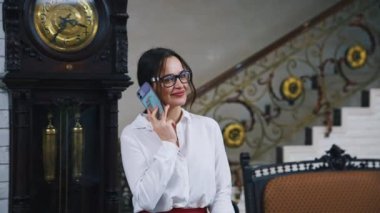 Telefonlu bir iş kadını portresi. Zarif gözlüklü çekici bir kız elinde bavuluyla otelde telefonla konuşuyor..