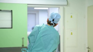 Hastane üniformalı doktor. Klinikteki koridordan ameliyathaneye bakan adam. Arka görünüm.