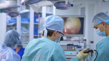 Büyük monitörün arka planında tıbbi ekip var. Modern ameliyathanede cerrahi operasyon yapan asistanları olan profesyonel bir cerrah. Doktor hastanede ameliyat sırasında modern tıbbi ekipman kullanıyor..
