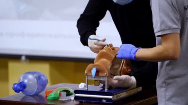Tıp öğrencileri için pratik beceriler. Eğitmen, pratisyen hekimin kuklanın burnuna tıbbi müdahale yapmasına yardım ediyor..