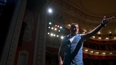 Sahnede el kol hareketi yapan ve konuşan bir adam var. Profesyonel aktör, sahne ışıkları altında tiyatrodaki rolünü oynuyor. Sahneden görüntüle.