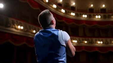 Adam sahnede prova yapıyor. Aktör sahne performansı sergiliyor ve modern tiyatro arka planında çok şey anlatıyor. Arka görünüm.