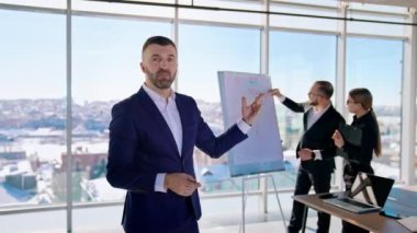 Ofisteki yöneticinin portresi. Pencere kenti geçmişiyle ilgili yeni planlar üzerinde çalışan iş adamları. Takım elbiseli yakışıklı iş adamı kamerada konuşuyor..