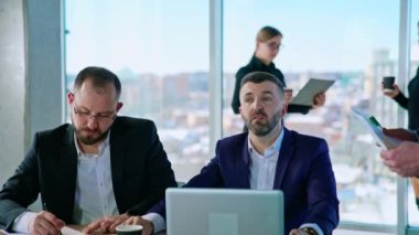 İçerideki iş adamları. Seçkin kostümlü başarılı girişimciler ekibi ofis odasında sohbet ediyor. İş bölgesi panoramik pencere görünümü.