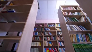 Kütüphane kitapları raflara istiflenmiş. Kütüphanede kitapları olan sıra sıra kitaplıklar. Eğitim, okul veya üniversite öğrenme konsepti. Kamera geri gider.