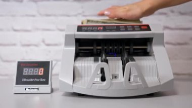 Elektronik nakit sayma makinesi. Banka hesapları ve dolar banknotları. Kadın eli, faturaları saymak için otomatik ekipmana kağıt para koyar..