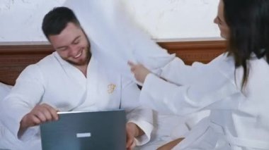 Oteldeki yatakta mutlu bir çift. Gülümseyen kadın kocasını yastıkla dövüyor. Bilgisayarı olan yakışıklı bir adam. Beyaz bornozlu çift birlikte eğleniyor..