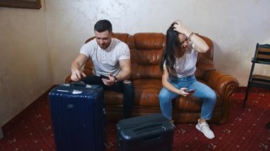 Kanepede bavulların yanında telefonları olan çift. Genç kadın ve erkek otelden ayrılmayı bekliyor ve cep telefonlarıyla oynuyorlar..