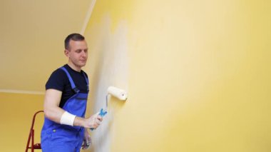 Oda makyajı. Duvarı boyayan genç bir adamın portresi. Duvarı yeni bir renge boyayan bir işçi. Kapalı alandaki bir merdivenden çıkan boya silindiriyle..