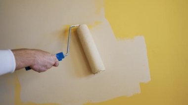 Kremsi boyayla sarı duvarı boyayan bir paten. Bir işçinin eli odayı açık renklerle dekore ediyor. Yakın plan. Makyaj konsepti.