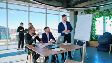 İş adamlarıyla panoramik ofis manzarası. Genç girişimcilerden oluşan bir takım erkek ve kadın çalışıyor. Ofis pencerelerinden şehir manzarası.