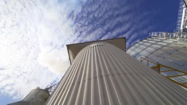 Gökyüzü arka planında metal tahıl asansörü. Tahıl depolamak için büyük bir ambar. Endüstriyel fabrikadan çıkan yoğun duman. Kirlilik. Aşağıdan görüntüle.