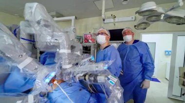 Klinikte robot cerrahisi. Robotla ilgili tıbbi operasyon. Tıbbi üniformalı ve maskeli konsantre doktorlar ameliyat sırasında geleceğe bakarlar. Minimum invazif robotik cerrahi.