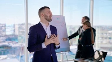 Sakallı iş adamı iş projesinden bahsediyor. Ofisteki bir girişimcinin portresi. Bir şehir manzarası ile panoramik pencere görünümü üzerinde çalışan iş arkadaşları.