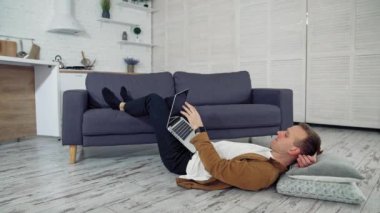 Freelancer yerde dizüstü bilgisayarda çalışıyor. Yorgun genç iş adamı yerde yatıyor ve evdeki uzun işten sonra dizüstünü bir kenara atıyor. Karantina sırasında uzak iş.