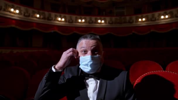 快乐的演员摘下医疗面具扔掉了 身穿服装的男人坐在空荡荡的剧场大厅里 兴高采烈地邀请人来表演 大流行病的结束 — 图库视频影像