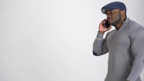 年轻的非洲裔美国人在电话里说话 身穿蓝色帽子和灰色毛衣的黑人 在白色工作室背景下讲着智能手机 概要视图 — 图库视频影像