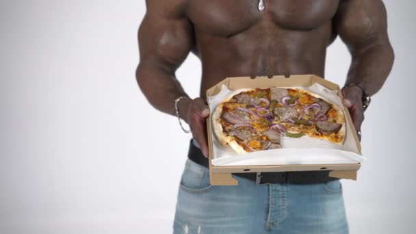 非洲男人手里拿着美味的披萨黑皮肤 肌肉发达的家伙提议在工作室背景下在纸盒里送披萨 — 图库视频影像