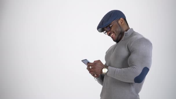 黒肌のスタイリッシュな男性はスマートフォンを使用しています キャップとメガネのアフリカ人男性のプロフィールビュー 携帯電話でメッセージを入力し — ストック動画