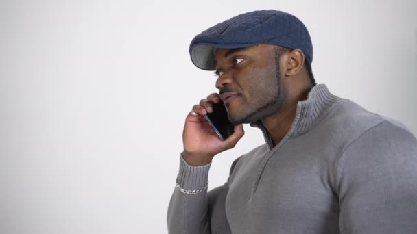 严重的非洲裔美国人讲电话 年轻的黑人 戴着蓝色时髦的帽子 穿着灰色的毛衣 在被白色隔离的手机上交谈 概要视图 — 图库视频影像