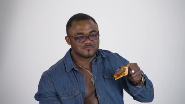 幸せなアフリカ人男性の肖像画 白いスタジオのバックグラウンドで美味しいピザを食べるメガネの黒人男性 不健康な食事を楽しむ — ストック動画