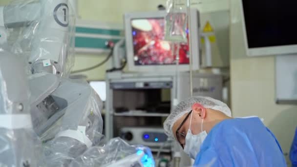 外科ロボットによる外科手術 現代のオペレーティングルームで医療服とマスクの若い外科医の肖像画 — ストック動画